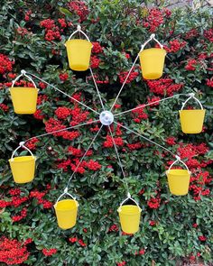 several yellow buckets hanging from a wire in front of red flowers and shrubbery