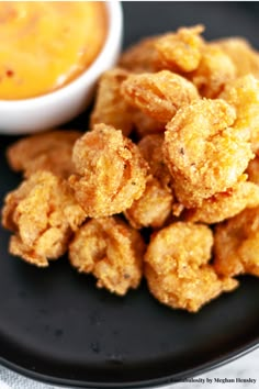 some fried food on a black plate next to a bowl of dip and dipping sauce