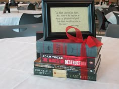 a stack of books sitting on top of a table next to a framed book with a red ribbon