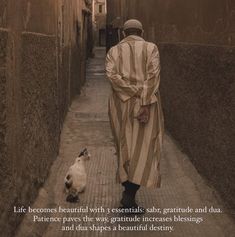 a man walking down a narrow street next to a white and black cat on the sidewalk