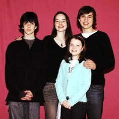 a group of people standing next to each other in front of a red wall with a pink backdrop