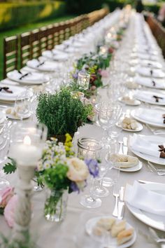 the long table is set with white and gold plates, silverware, and flowers