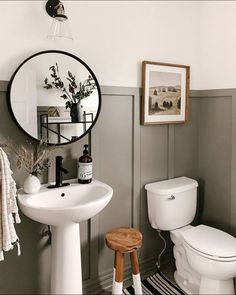 a white toilet sitting next to a bathroom sink under a round mirror on a wall