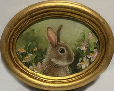 a painting of a rabbit in a gold frame with flowers on it's side