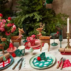 the table is set for christmas dinner with red and green plates, napkins, silverware and candlesticks