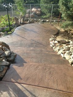 a concrete walkway with rocks and trees in the background