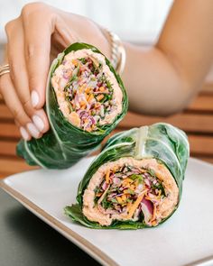 two wraps filled with meat and vegetables on top of a white plate next to a woman's hand