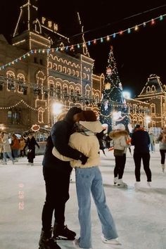 two people hugging on an ice rink in front of a lit up building at night