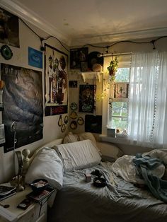 an unmade bed in a messy room with pictures on the wall and windows above it