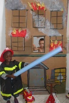 a young boy holding a large blue tube in front of a cardboard fire station scene