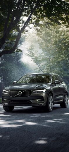 a silver volvo suv is driving down the road in front of some trees and bushes