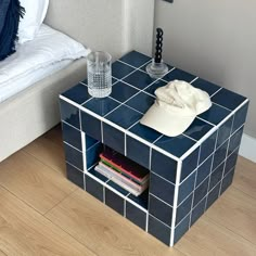 a blue tiled side table with a hat on top and magazines in the bottom drawer