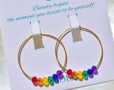 a pair of hoop earrings with colorful beads on each end and a card that says, beauty begins the moment you decide to be yourself