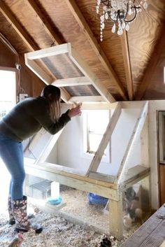 a woman standing next to a chicken coop in a room filled with wood planks