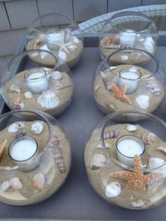 there are many candles and seashells in glass bowls on the table with sand