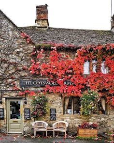 an old stone building with red leaves on the windows and flowers growing all over it