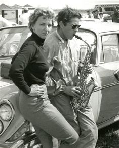 black and white photograph of two people standing next to a car with a saxophone in their hands