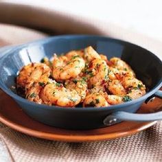 a blue bowl filled with cooked shrimp on top of a wooden table next to a fork