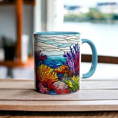 a colorful mug sitting on top of a wooden table next to a water view window