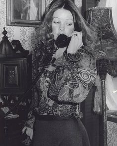 a woman talking on a phone while standing in front of a wallpapered room