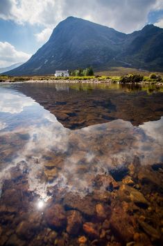 the sky is reflected in the still water at the bottom of the mountain range, with a house on the other side