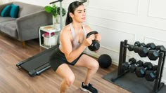 a woman is doing squats while holding a dumbbell in her hand and looking at the camera