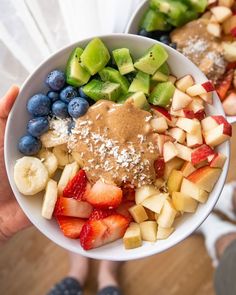 a person holding a bowl of fruit with peanut butter on top and blueberries in the bottom