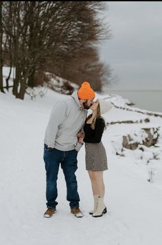 a man and woman are kissing in the snow near some trees, with water behind them