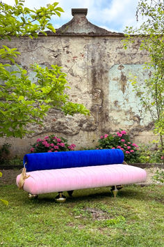 a pink and blue couch sitting on top of a lush green field next to a building