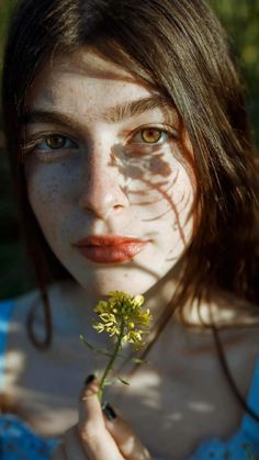 a woman with freckles on her face holding a flower in front of her face