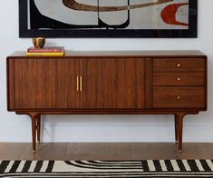 a painting hangs above a wooden cabinet in a room with striped rug and black and white carpet