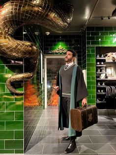 a man standing in front of a green tiled wall with a snake hanging from the ceiling