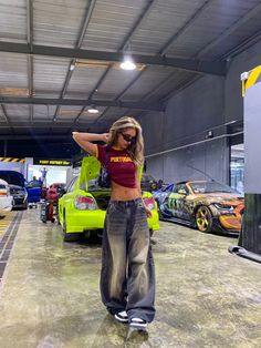 a woman standing in front of some cars with her hands on her hips and arms behind her head