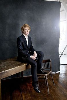 a man sitting on top of a wooden table next to a blackboard behind him