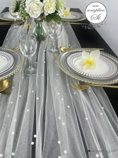 the table is set with silver and white plates, gold rimmed glasses, and flowers