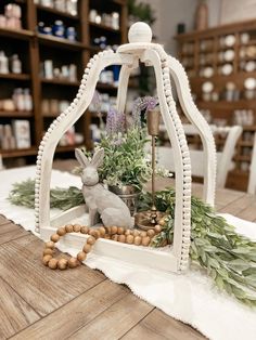 a small white birdcage filled with flowers and plants on top of a wooden table