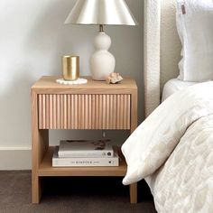 a nightstand with two books and a lamp on it next to a bed in a bedroom