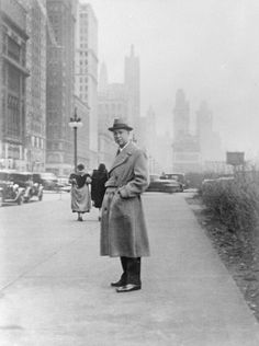 an old black and white photo of a man standing on the sidewalk