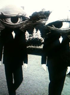 two men in suits walking down the street with large eyes on their heads and one wearing a top hat