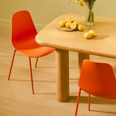 a wooden table topped with orange chairs next to a vase filled with flowers and lemons