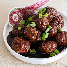 meatballs with green onions and sauce in a white bowl on a beige tablecloth