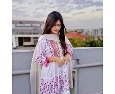 a woman standing on top of a roof wearing a white dress and pink bracelets