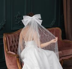 a woman in a white wedding dress sitting on a pink chair with a veil over her head