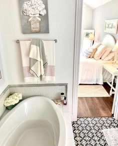 An elegant farmhouse bathroom with a large white tub framed by light gray walls is adorned with floral accents. Black and white tile bathroom flooring provides a pleasing contrast while accenting the rest of the bathroom decor. Light walls brighten the space and a clean towels hangs on a rod mounted above the tub...   Image: tarastexaslakehouse