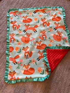 two baby blankets laying on the floor next to each other, one with a red and green fox design