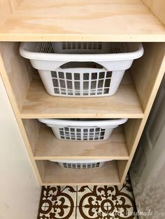 two white laundry baskets sitting on top of a wooden shelf next to a tile floor