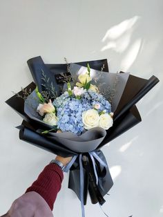 a bouquet of blue and white flowers is being held by a person's hand