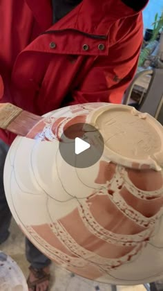 a man is holding a large vase in his hands and painting it with red paint