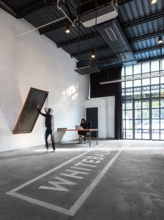 a man is holding up a large piece of art in an empty room with people sitting at tables