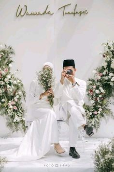 a man and woman sitting next to each other in front of a wall with flowers